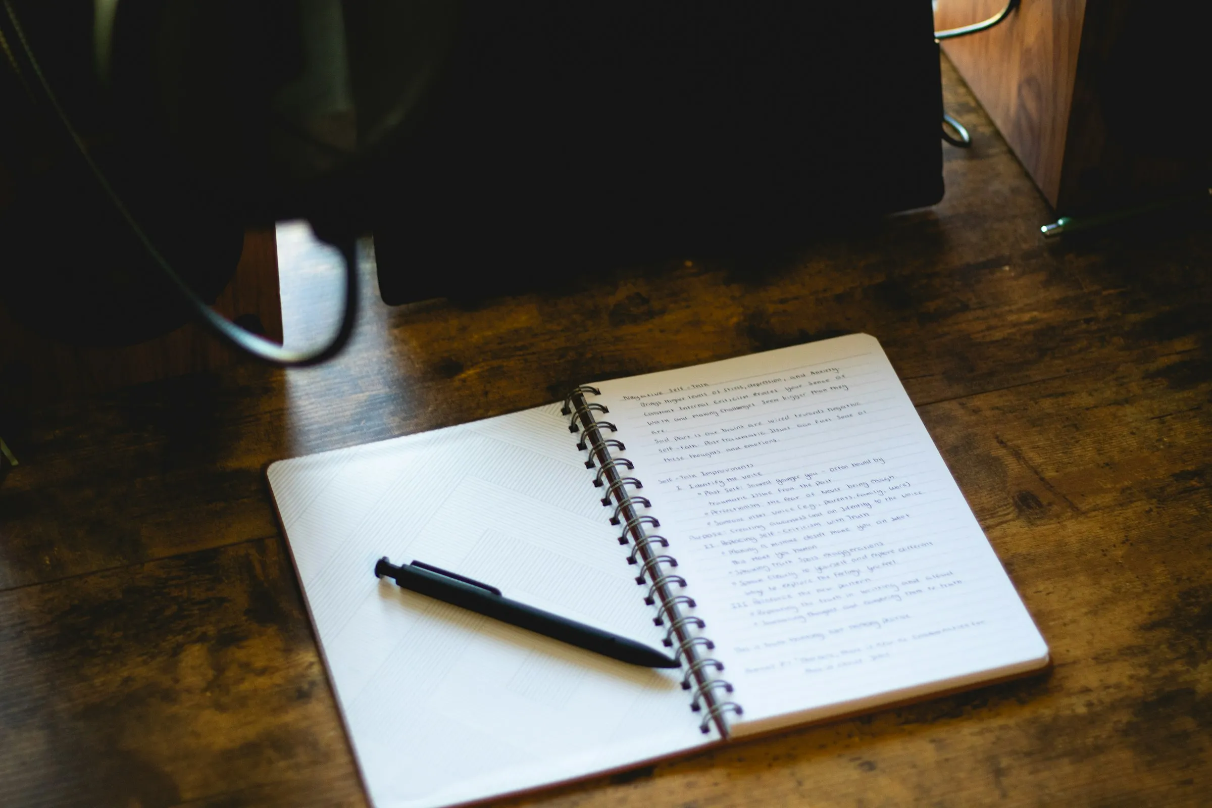 An open notebook with handwritten notes and a pen on a wooden desk.